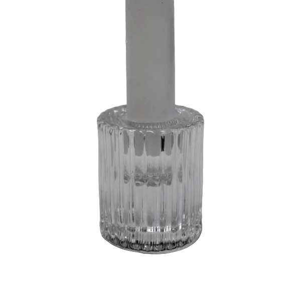 A clear ribbed glass candlestick holder base with a white candle inserted, photographed on a light fabric surface.