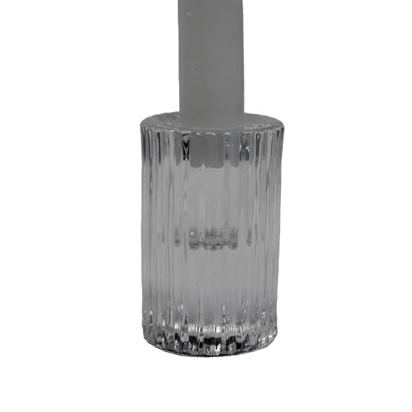 A clear ribbed glass candle holder or candle base with a white candle inserted, photographed against a soft light gray fabric background.